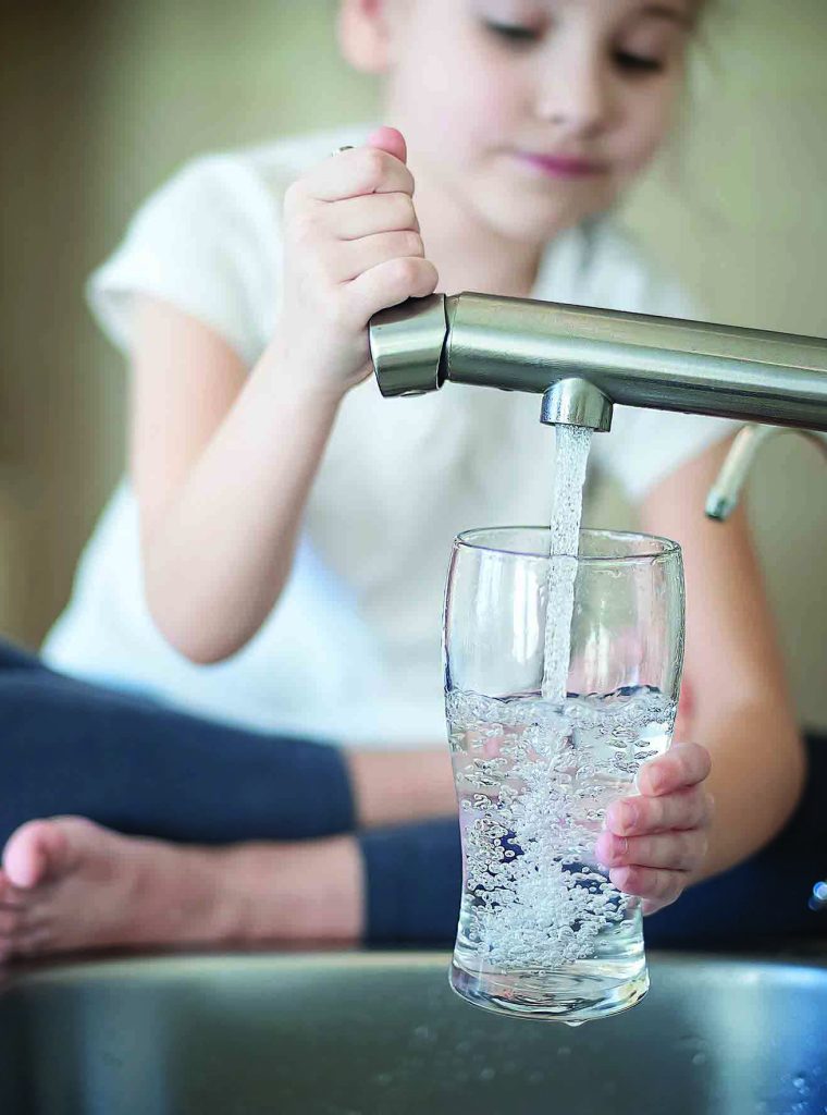 Little girl opens a water tap with her hand holding a transparent glass. Kitchen faucet. Glass of clean water. Filling cup beverage. Pouring fresh drink. Hydration. Healthcare. Healthy lifestyle.